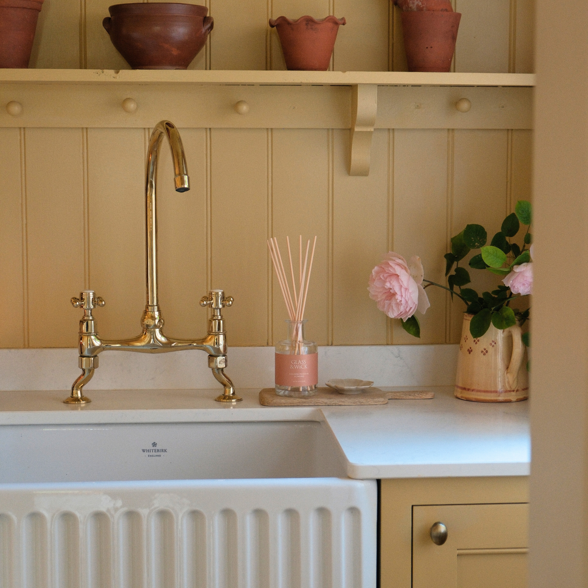 Reed diffuser displayed in kitchen sink area with gold faucet, decorative items, and a light-colored wall.
