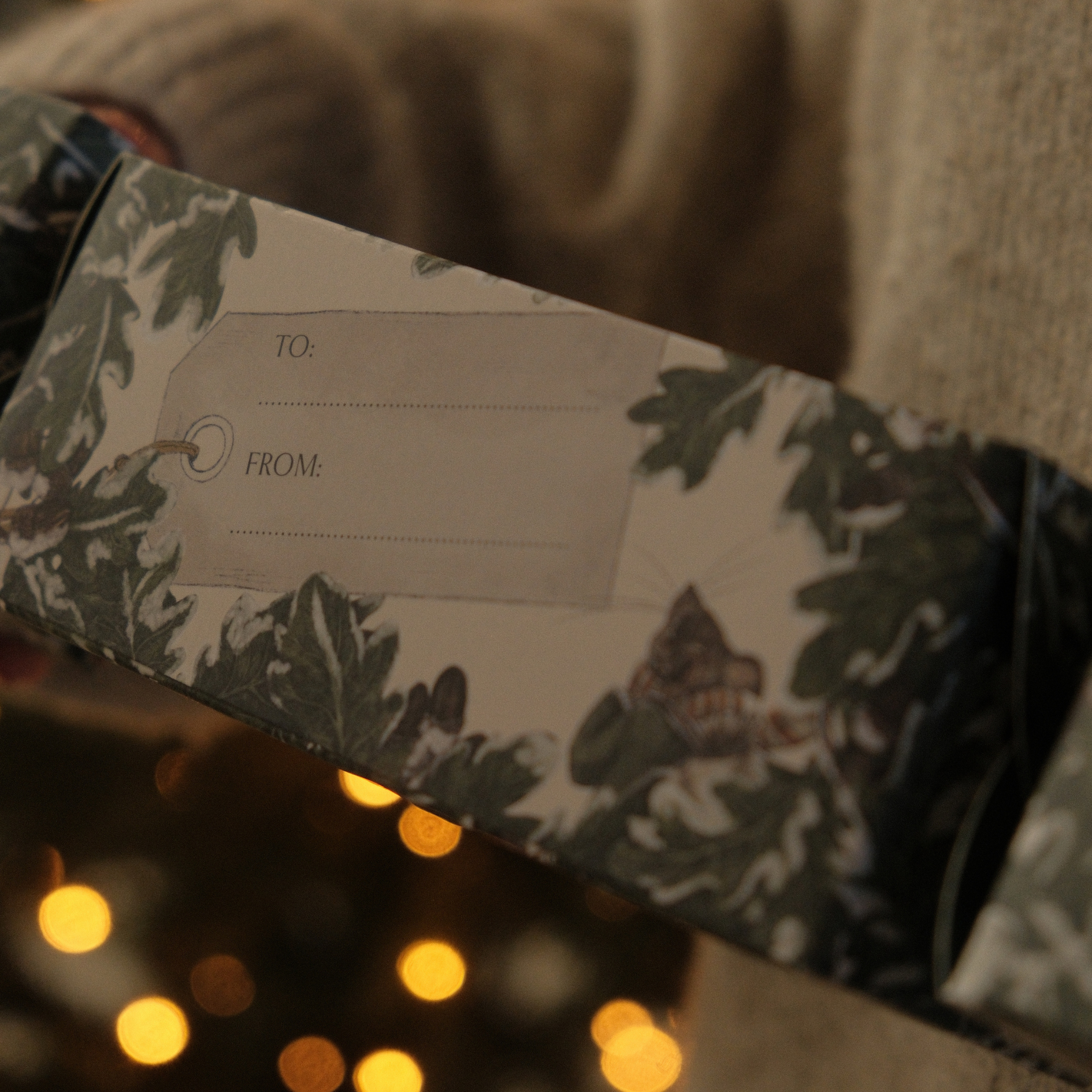 Glass & Wick christmas cracker with oak leaf design held by a person against a blurred background with lights