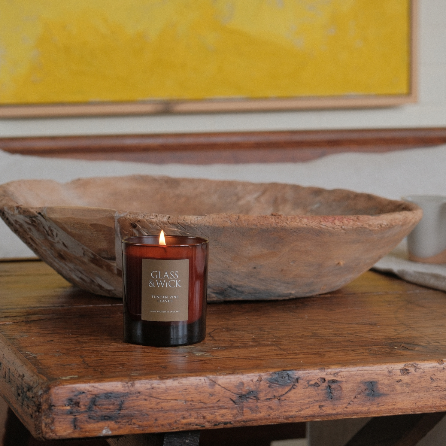 Glass & Wire candle on a wooden table with a rustic bowl and abstract painting in the background